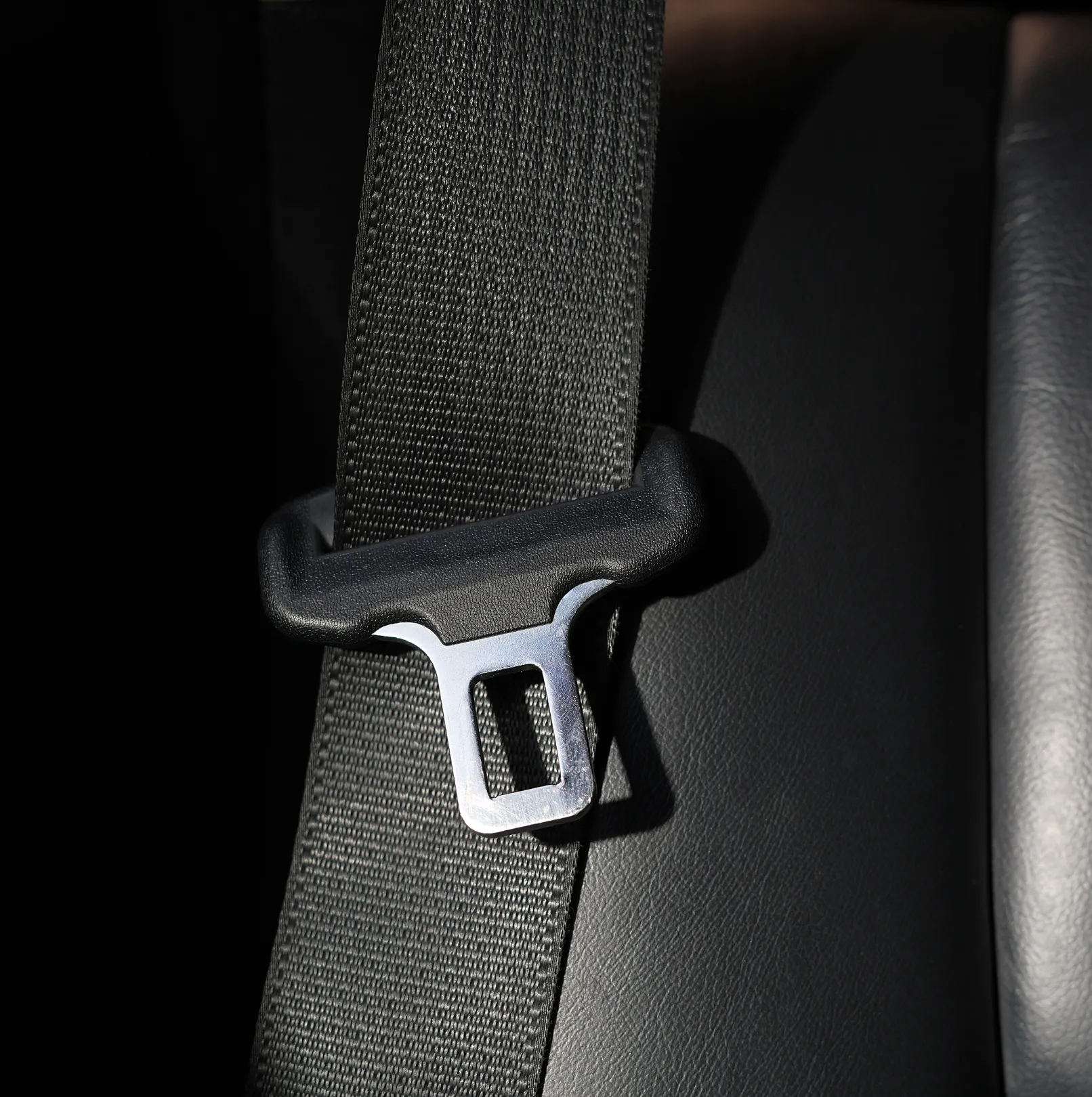 Close-up of a black seat belt webbing strap running through a plastic guide with a polished steel tongue plate resting against a vehicle seat.